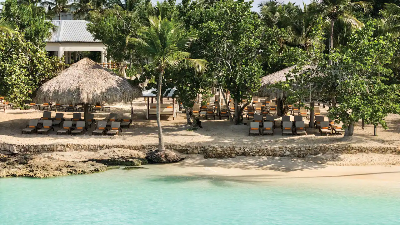 Beachfront lounge chairs and tropical palapas at Secrets La Romana Resort & Spa.
