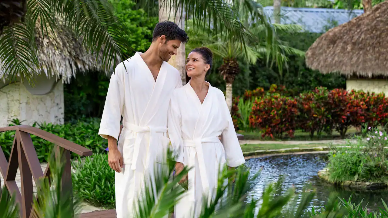 Couple in spa robes walking through tropical gardens at Secrets La Romana Resort & Spa.